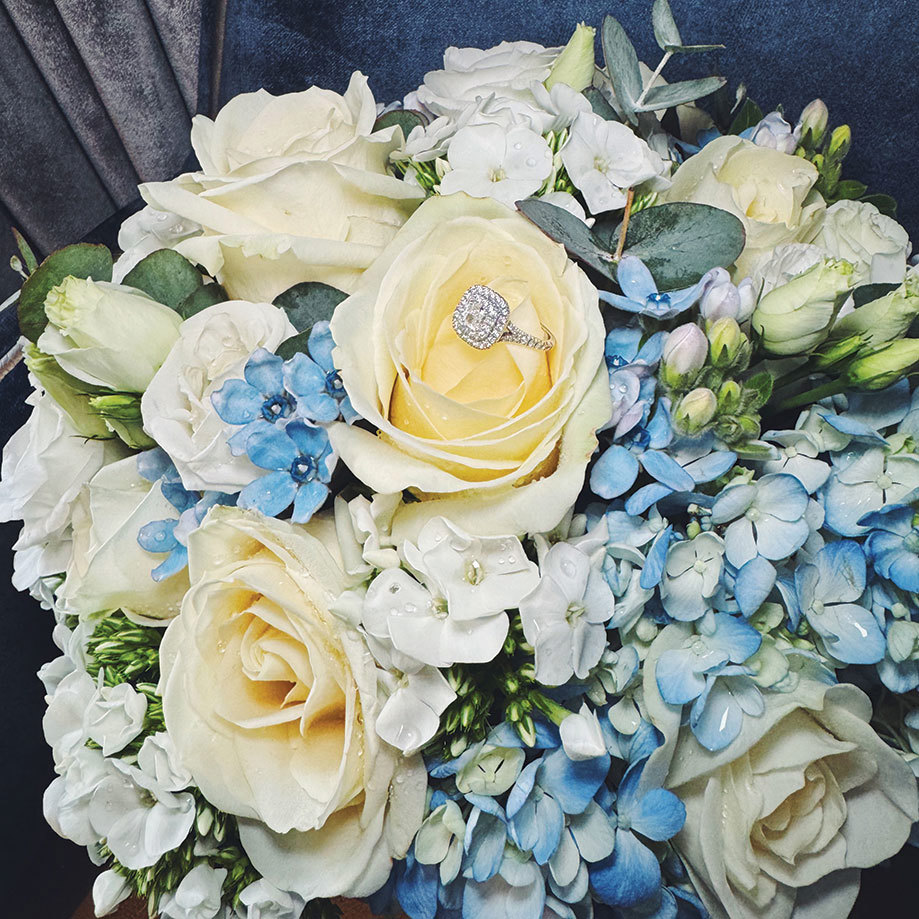 a blue and white bouquet of flowers with diamond engagement ring on a rose