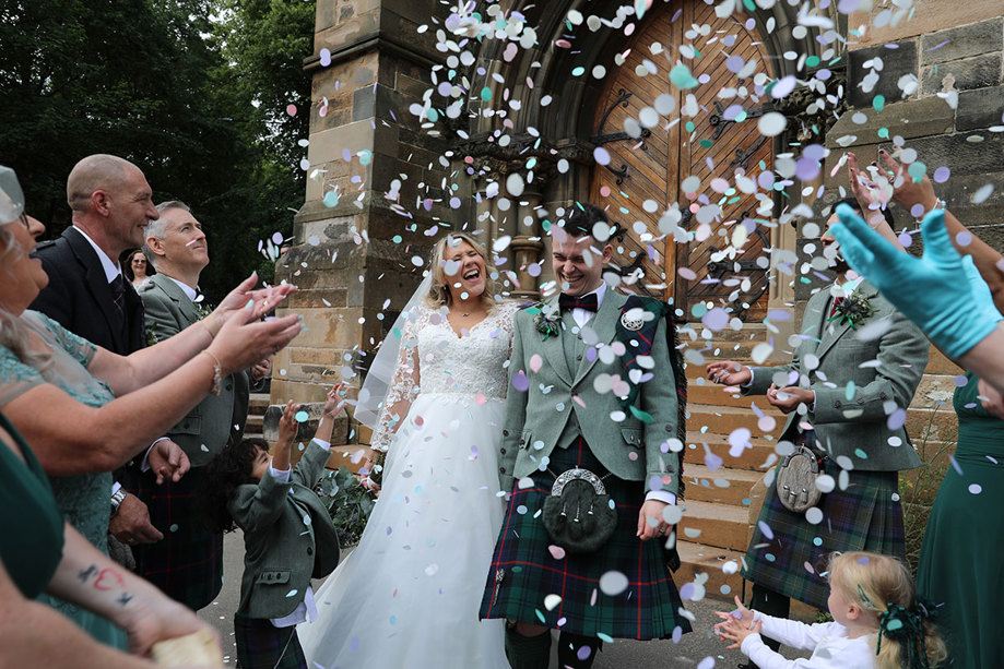 A bride and groom being showered in confetti by their guests as they leave a church