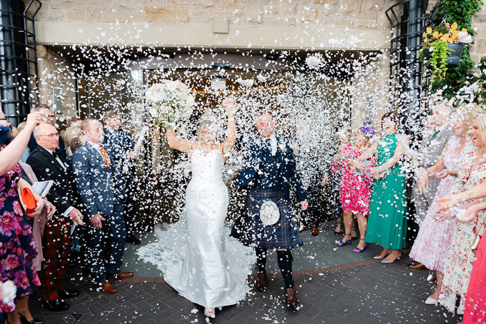 a bride and groom are showered in lots of white confetti outside the Old Course Hotel.