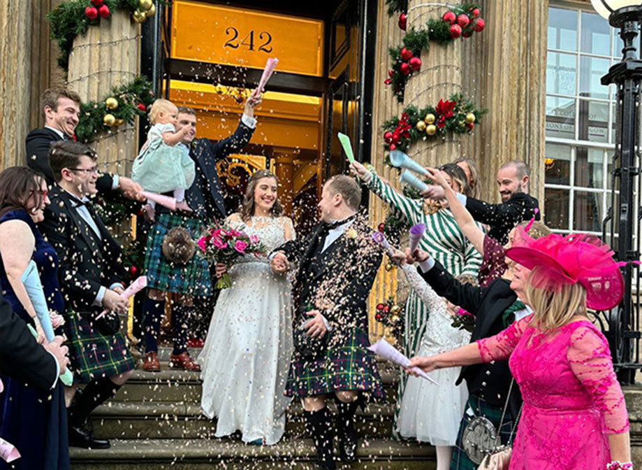 People throw confetti over a bride and groom as they walk down stone steps