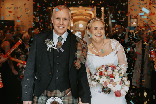 Bride and groom are covered with confetti and smile for the camera