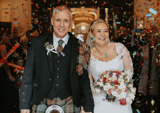 Bride and groom are covered with confetti and smile for the camera