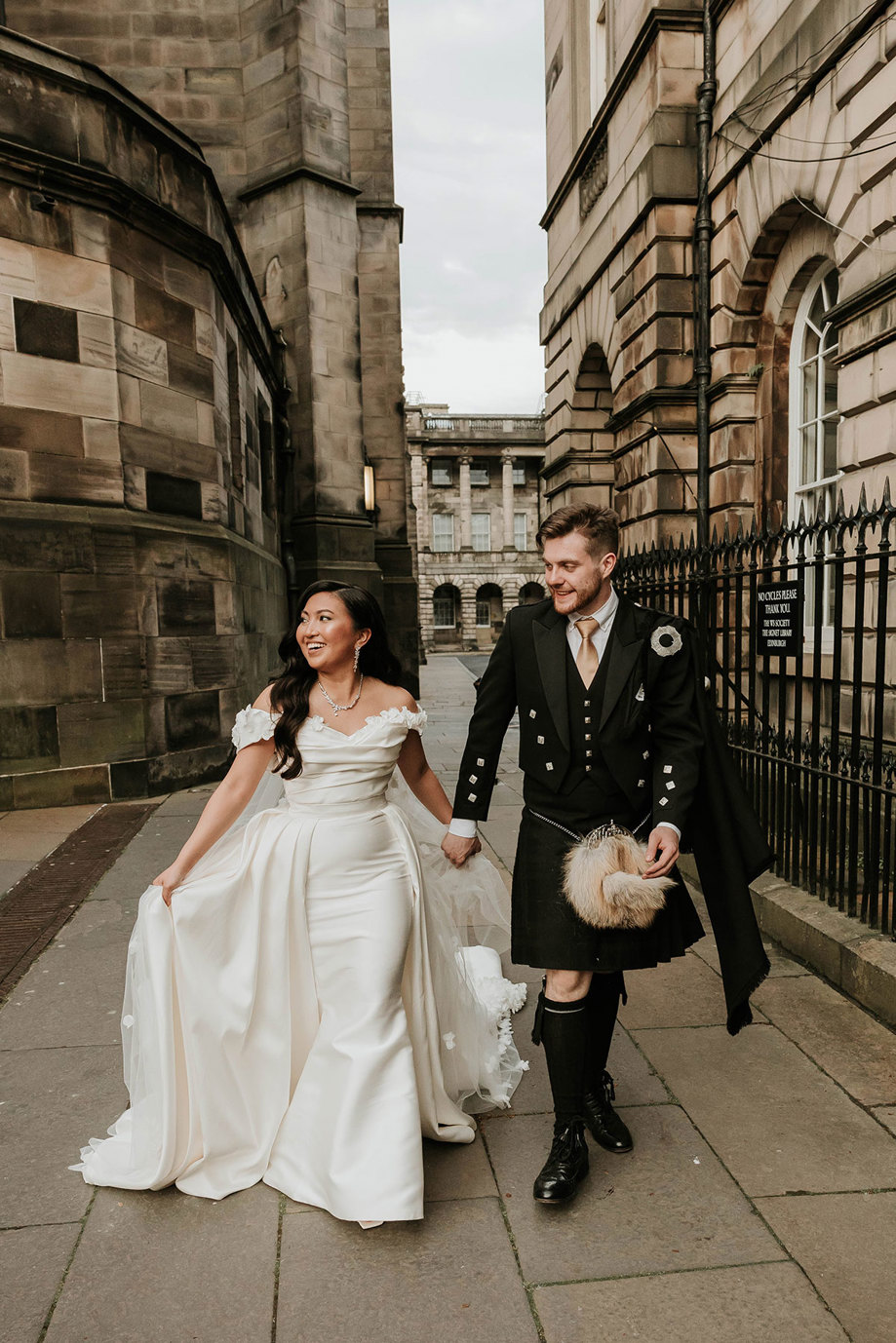 bride and groom walking through edinburgh city centre in wedding outfits