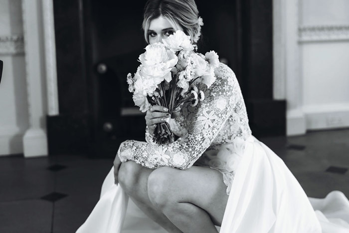 black and white image of a woman holding a bouquet up to her face while crouching down in a long sleeve floral flowy dress