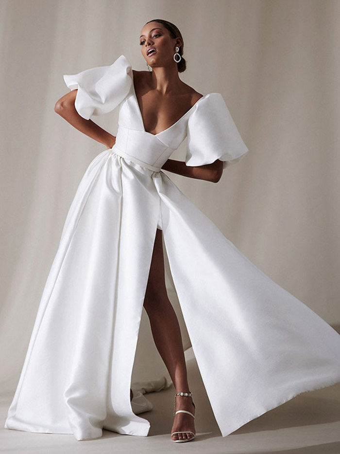 front facing woman wearing long white wedding dress with high leg slit, v-neck and large puff sleeves