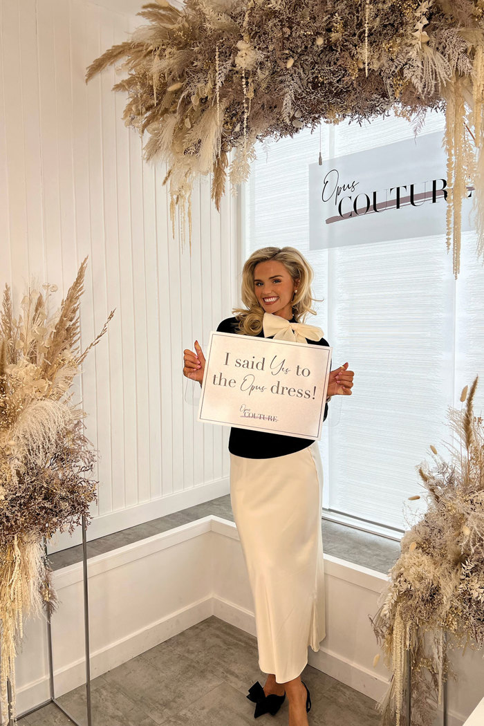 A person holding a sign that reads 'I said yes to the dress at Opus Couture'