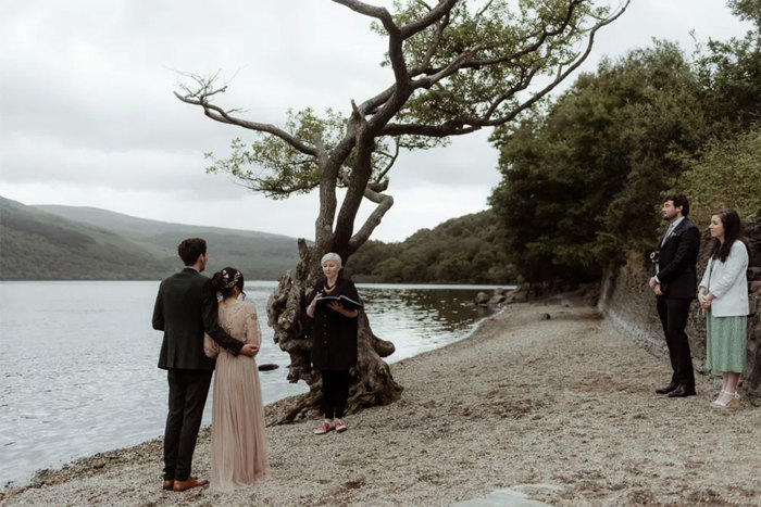 couple getting married in front of witnesses and celebrant on beach next to water