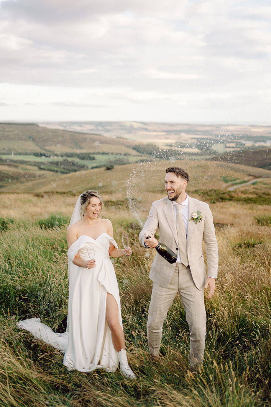 couple laugh at top of Cairn o'Mount with champagne