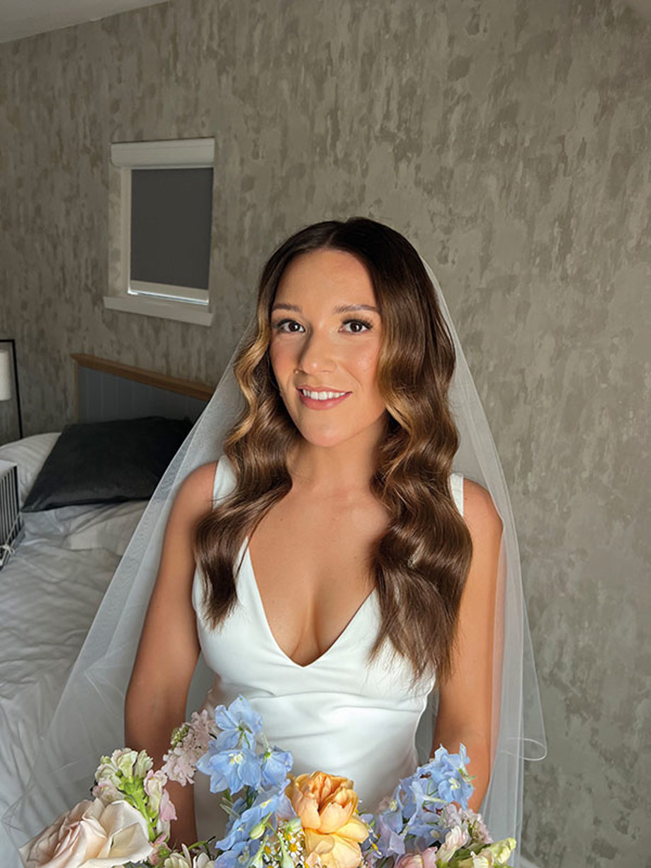 brunette bride holds pastel bouquet and smiles in her wedding dress and veil