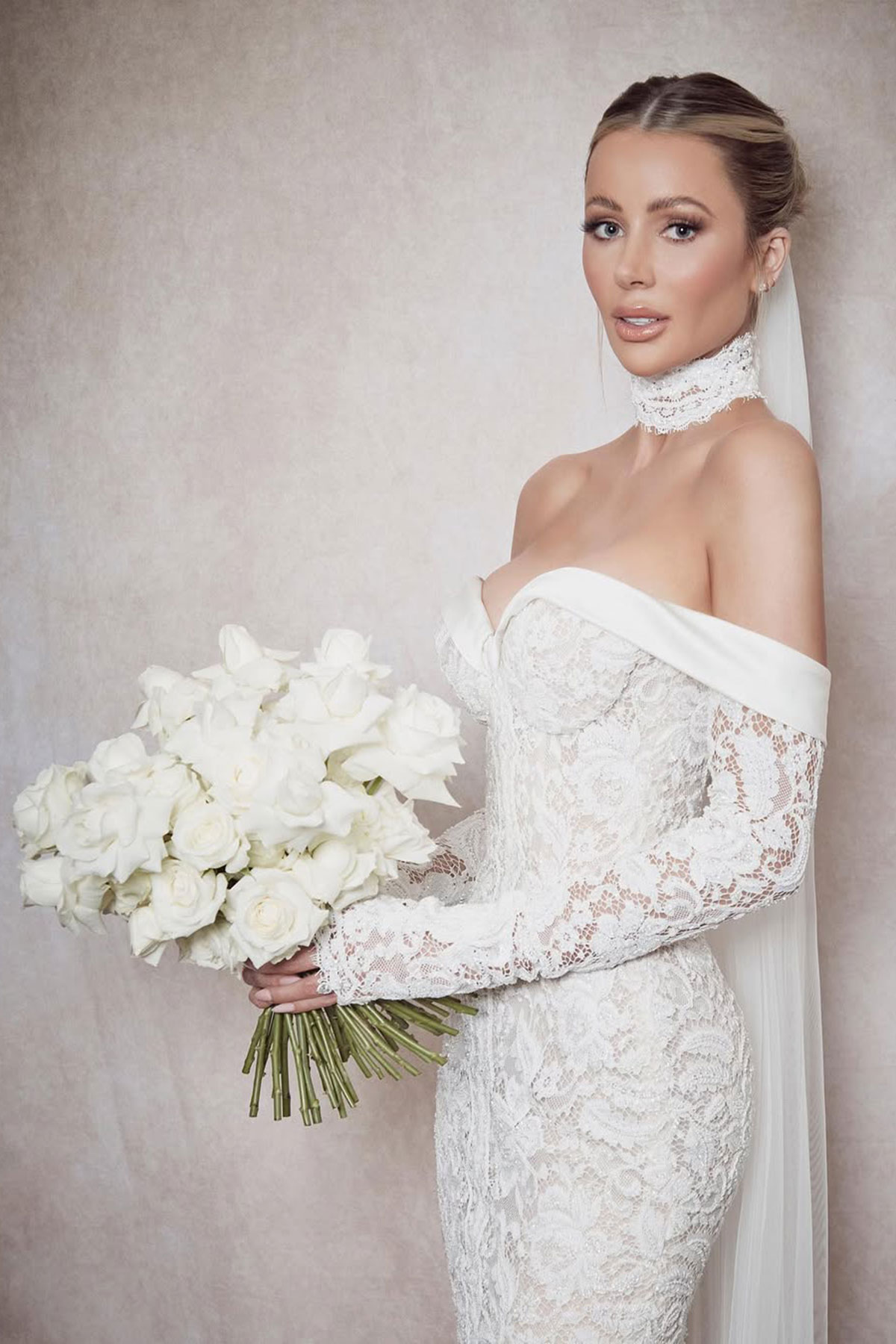 portrait of a bride with a lace off the shoulder wedding dress with matching lace choker holds a large bouquet of white roses out in front of her
