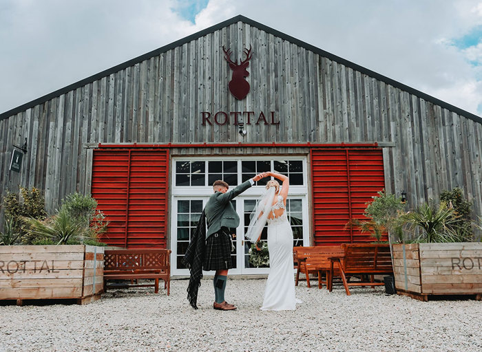 a groom twirling a bride outside the wooden clad exterior of Rottal Steading in Angus