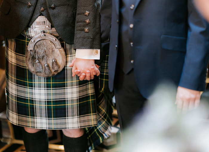 detail of a man in a kilt holding hands with a man in a blue suit