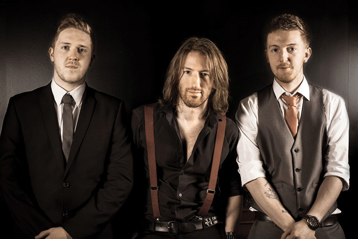 Three men standing in a row wearing dark suits and ties