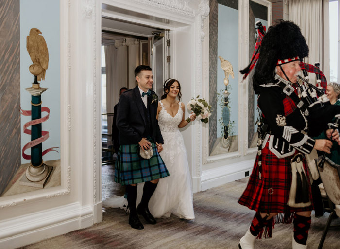 Couple walking behind man playing bagpipes