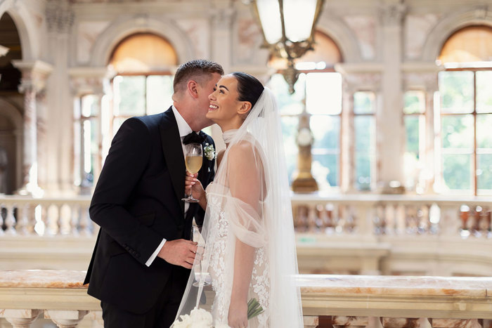 A person in a white dress holding a glass of champagne with a person in a black tuxedo at Gosford House.