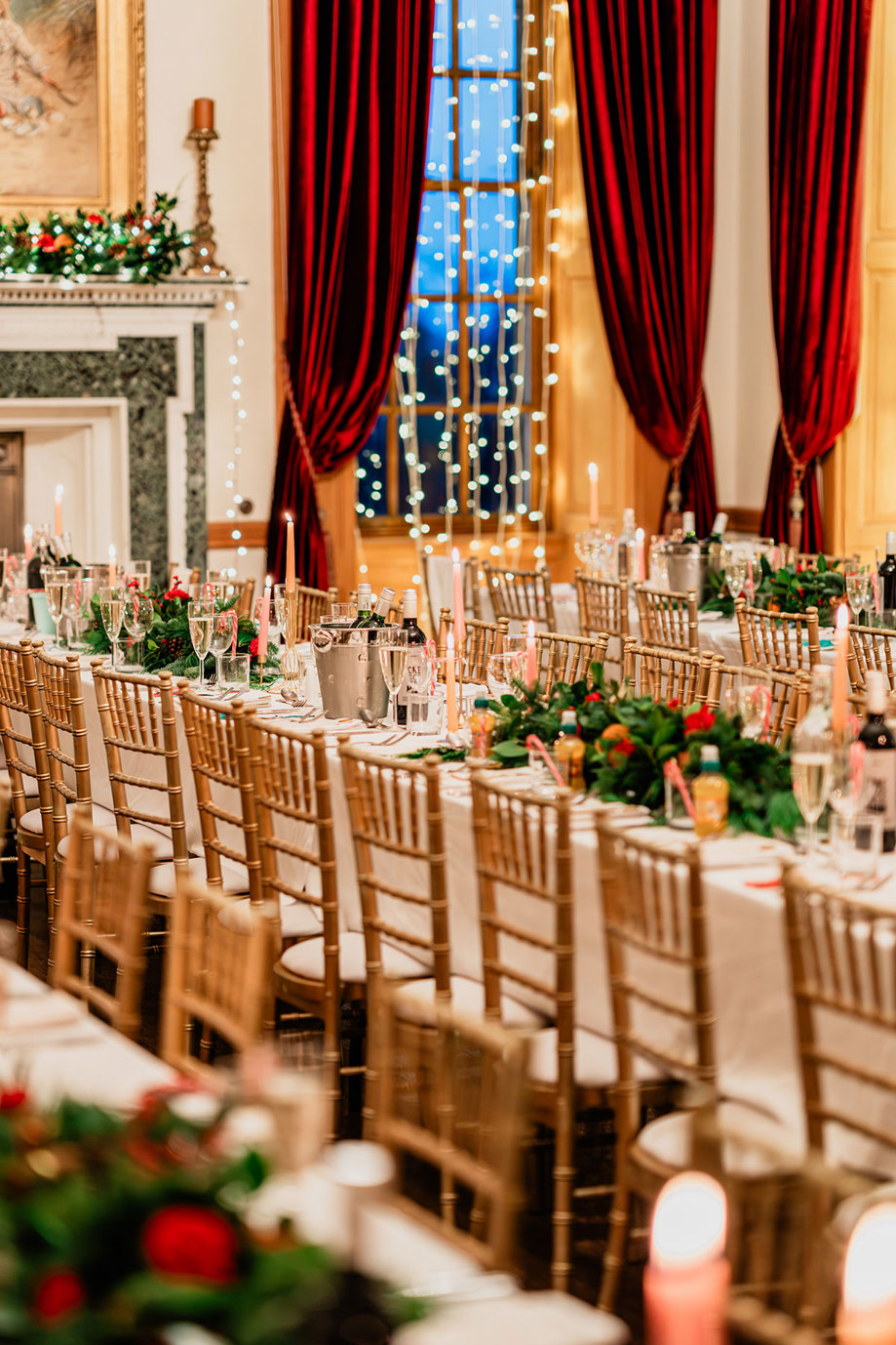 long decorated dining tables include red and green foliage centrepieces, pale pink and orange tapered candles, plus buckets of wine and glasses of champagne