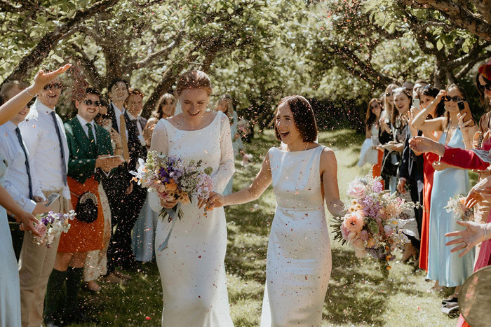 two brides walking through a confetti shower during outdoor wedding at the Byre at Inchyra