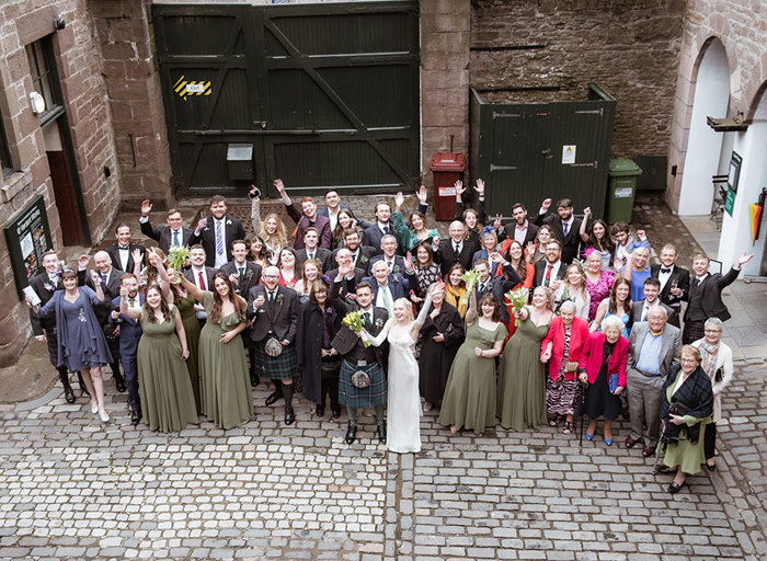 an aerial group photo of people in a cobbled courtyard with their arms in the air at a wedding