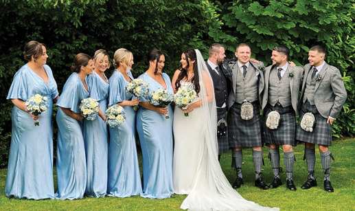 Five bridesmaids in blue, bride, groom and three groomsmen standing in row