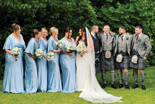 Five bridesmaids in blue, bride, groom and three groomsmen standing in row