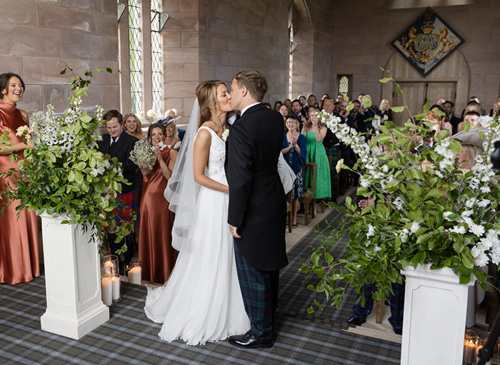 bride and groom kissing at top of aisle with flowers and guests