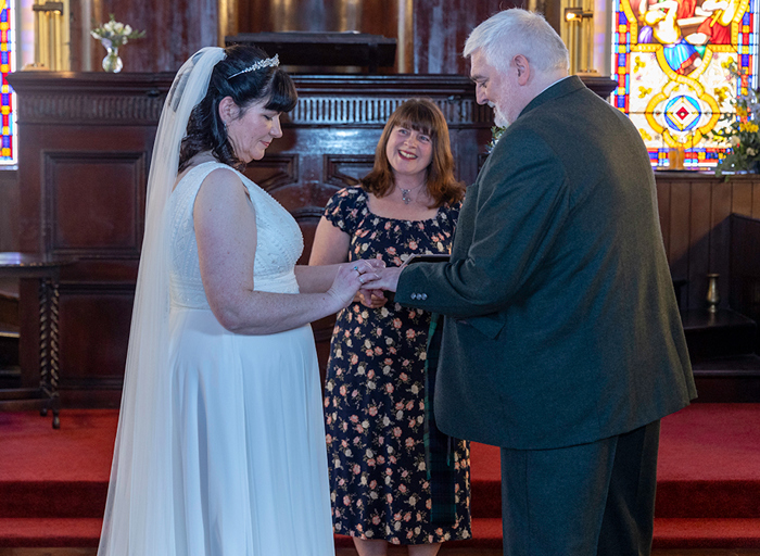 a wedding celebrant standing between a bride and groom as they exchange rings in a church setting