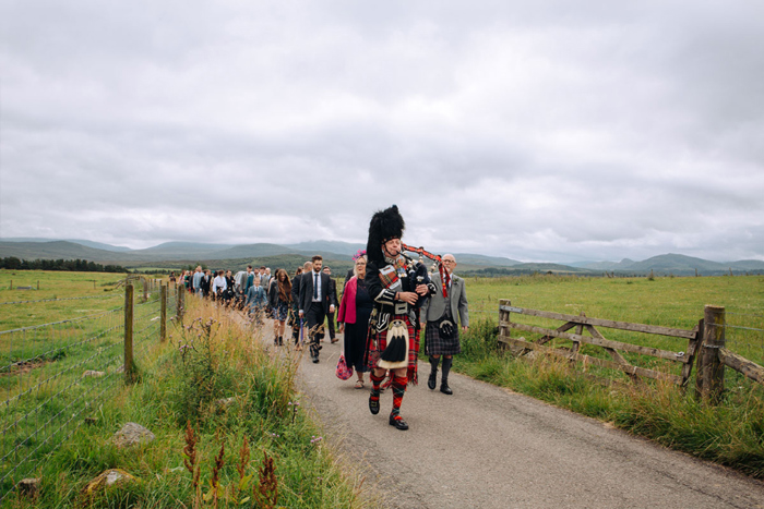 A Bagpiper Leading Wedding Guests On A Road