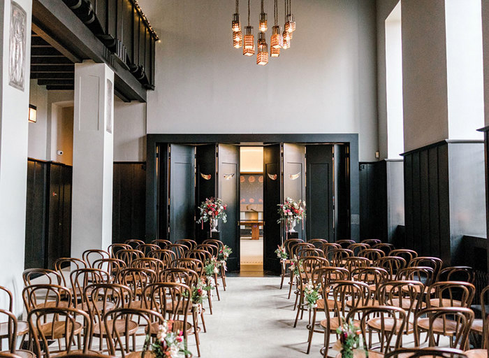 an Art Noveau style room with wooden panelling set with rows of wooden chairs for a wedding ceremony