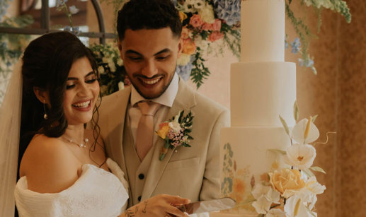 A bride and groom smile as they cut into their four tier wedding cake