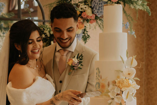 A bride and groom smile as they cut into their four tier wedding cake