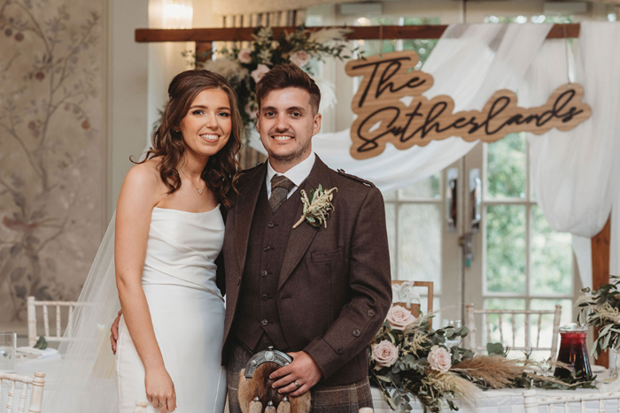 Couple smile in front of sign reading 'The Sutherlands'