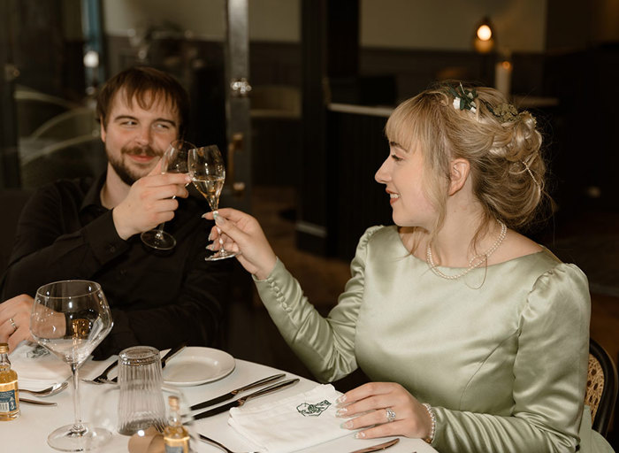 a bride and groom toasting with champagne flutes while seated at dinner