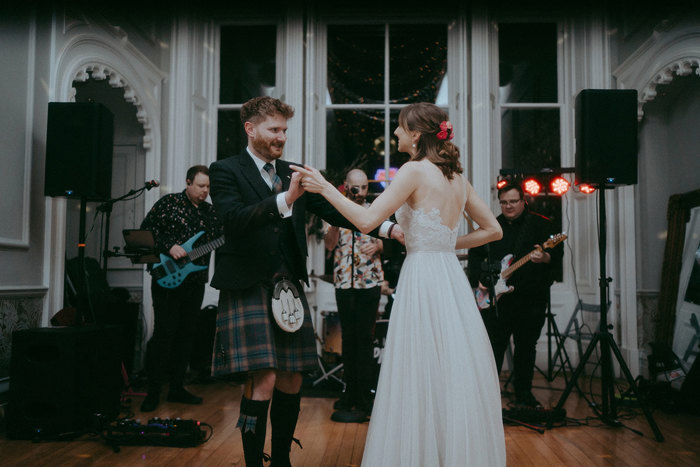 first dance of a bride and groom in front of a large window at Netherbyres House as a band perform in background