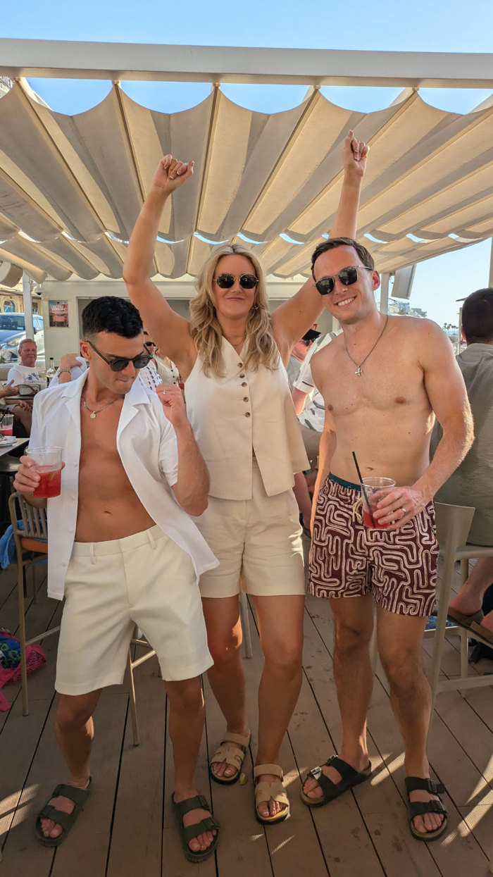 three people wearing summer clothes and sunglasses dancing under a sun shade