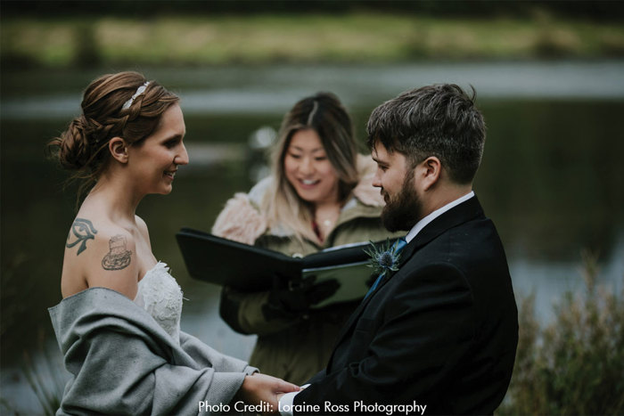 Bride and groom hold hands with celebrant visible in the background