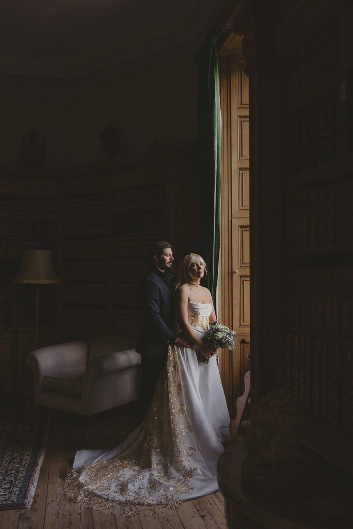 A bride and groom standing by a window