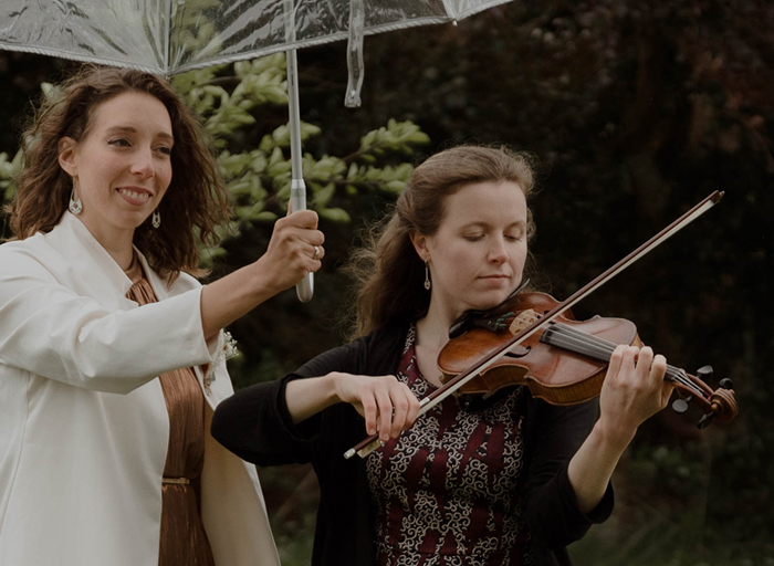 two people standing under a clear umbrella, one of whom is playing the violin