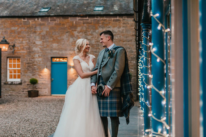 A bride and groom stand in a courtyard smiling at each other