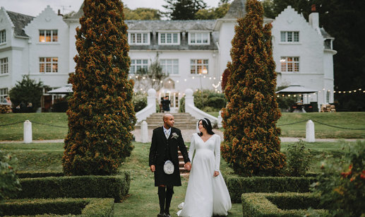 A person in a kilt and person in a wedding dress holding hands and walking in a garden at Achnagairn Castle.