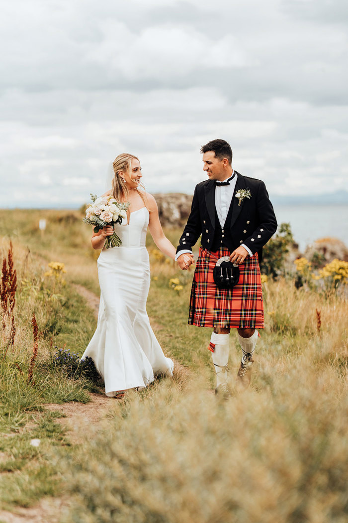 A bride and groom holding hands and walking in a field.