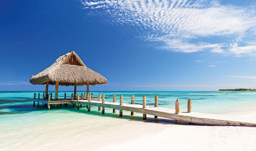 a dock with a straw roof on the water next to a white sand beach