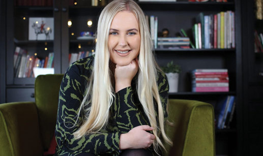 blonde smiling woman rests her fist under her chin while sat on green chair