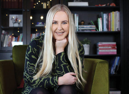 blonde smiling woman rests her fist under her chin while sat on green chair