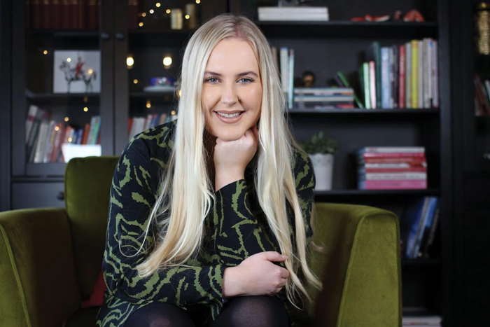 blonde smiling woman rests her fist under her chin while sat on green chair