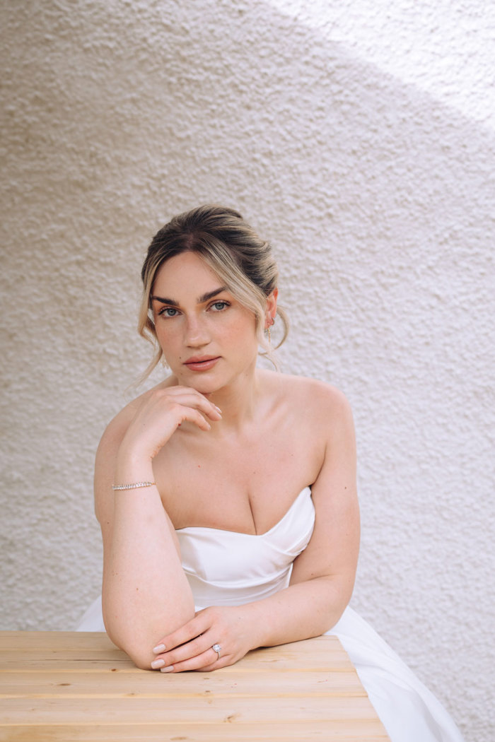 closeup of bride in strapless wedding dress, her one hand resting under her chin and strands from her updo framing her face 