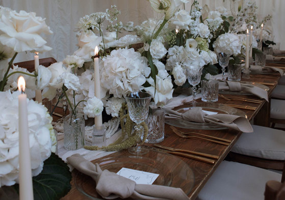 long wooden table set with clear charger plates, linen napkins, and a long middle section filled with white flowers and crystal glassware