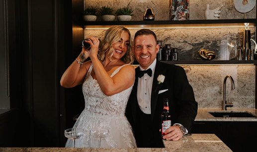 A bride and groom posing for a picture while making a cocktail.