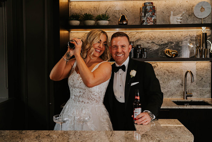 A bride and groom posing for a picture while making a cocktail.