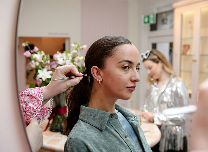 A woman facing side on had an earring held up to her ear 