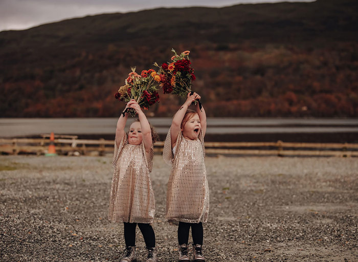 two young girls wearing gold sparkly dresses raising bunches of flowers above their heads